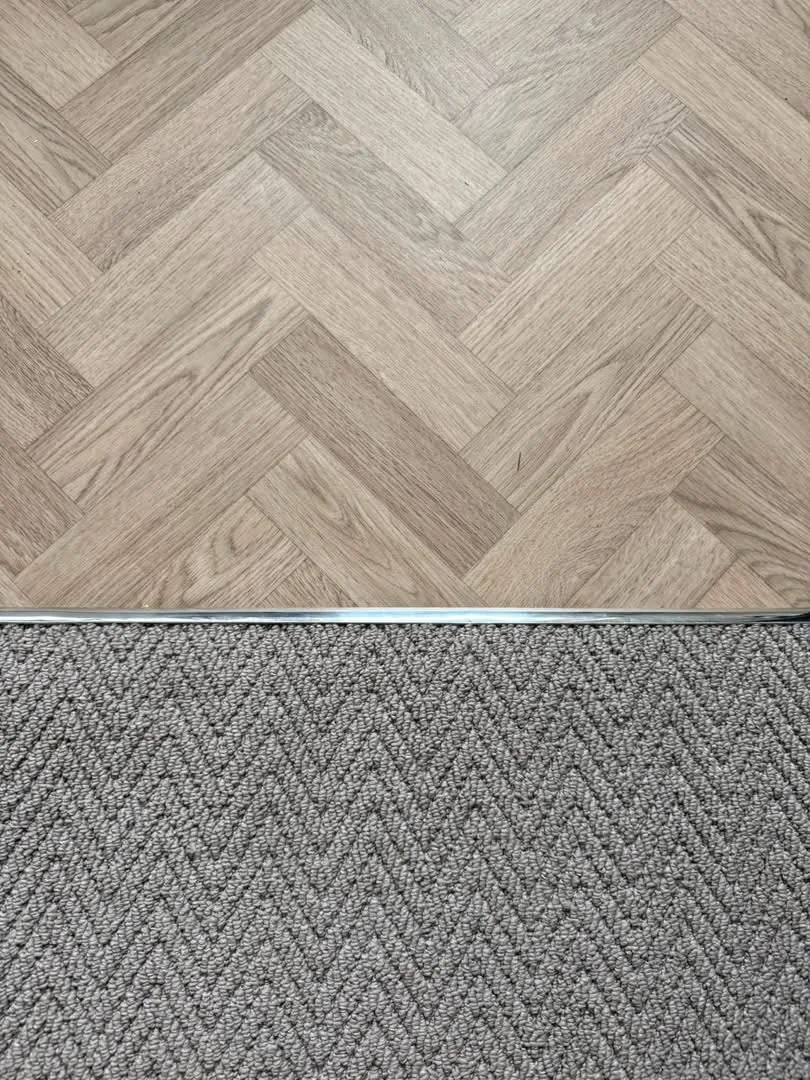 Close-up of herringbone vinyl meeting carpet at a metal threshold, Signature Carpets and Flooring, Greater Manchester